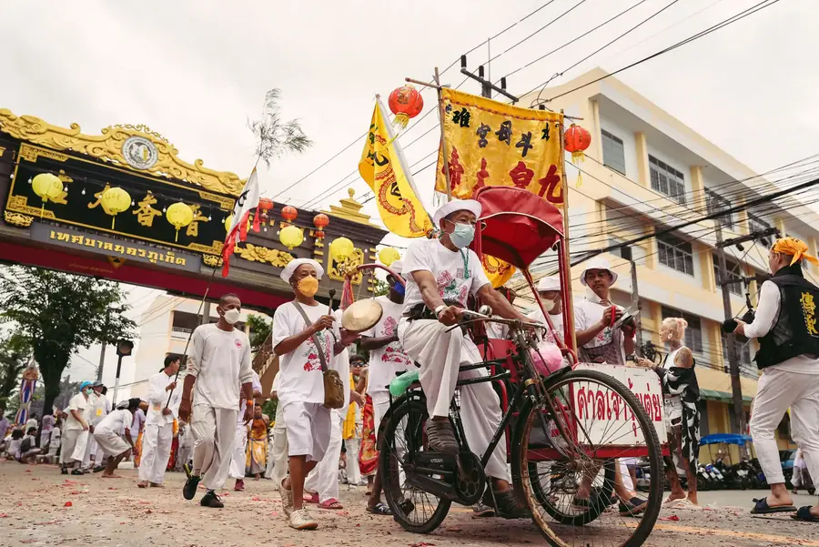 Procession in white through a Phuket street under red lanterns and festival banners
